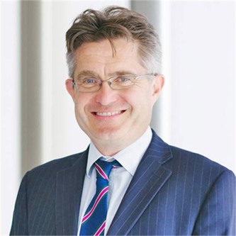 Charles Staveley in a pinstripe suit and tie, in front of a pale background