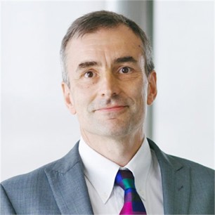 Charles Pigott in a grey suit and tie, in front of a pale background