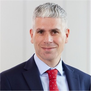 Adrian Kwintner in a blue suit and tie, in front of a grey background